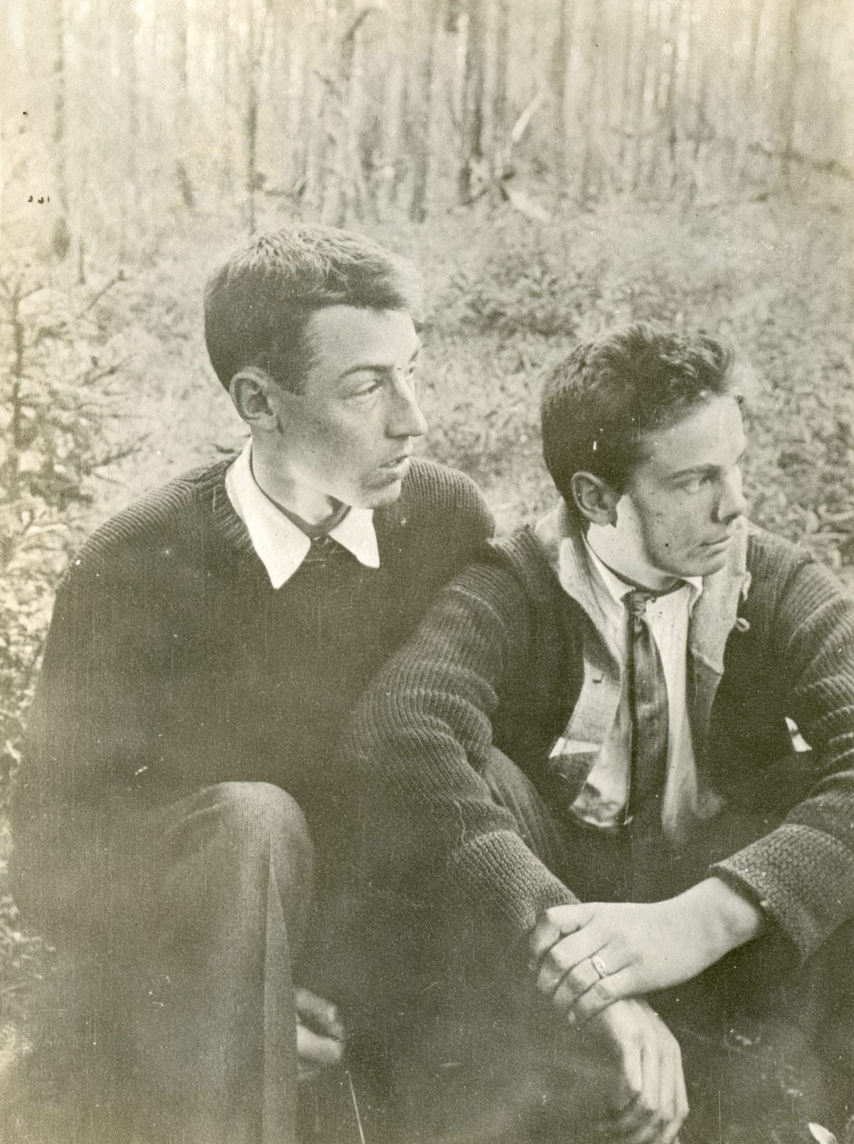Len and Cub sit close together among trees in knitted sweaters, collared shirts and ties; a hand rests over a forearm.