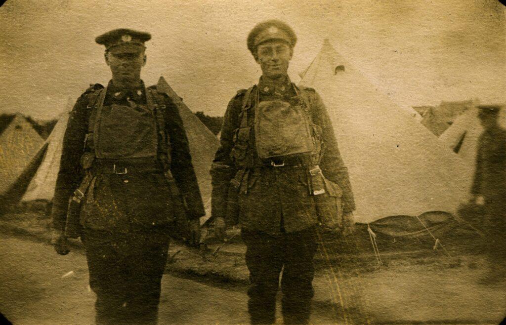 Len and Cub stand side by side in military uniforms, caps and field equipment, with canvas tents behind them.